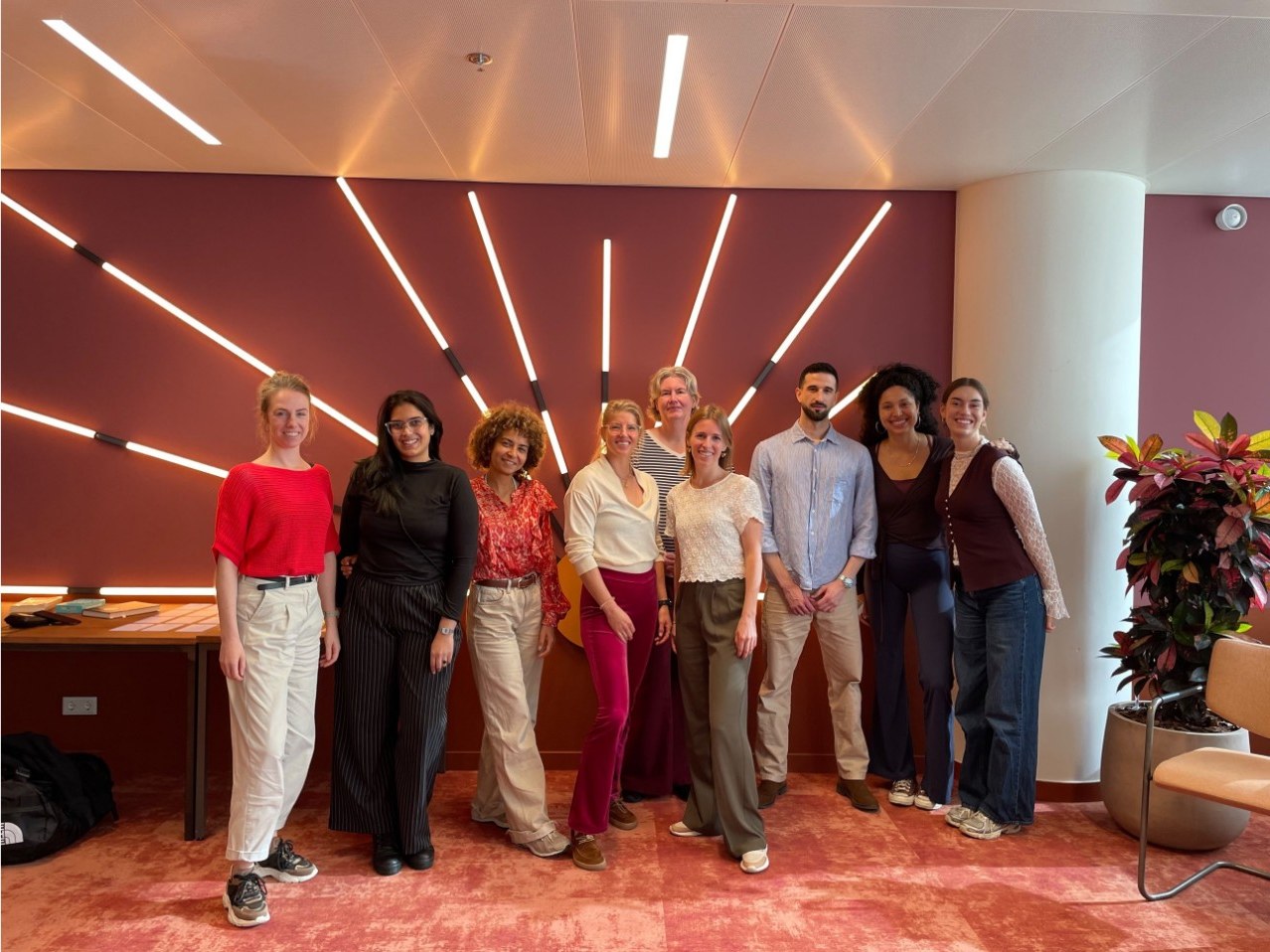 Marjolein van der Krol with the participants of the workshop at Wonders of Work, standing in front of a wall of sunburst lights